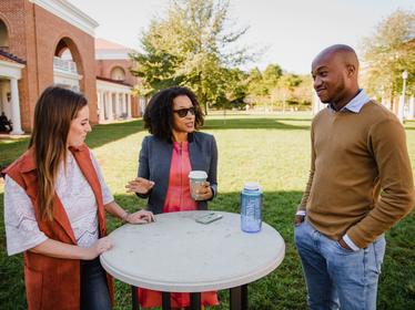 two students and a faculty member talk at an outside table