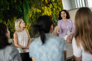 Female business leader speaking to a group of students or professionals at Darden School of Business, fostering mentorship and leadership development in a modern, green-designed space