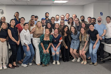Group photo of business school students and professionals smiling together in a classroom setting.